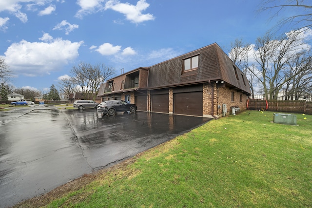 view of side of home featuring roof with shingles, mansard roof, brick siding, a garage, and a lawn