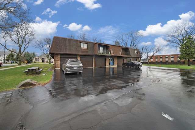 exterior space featuring driveway, brick siding, mansard roof, and a front yard