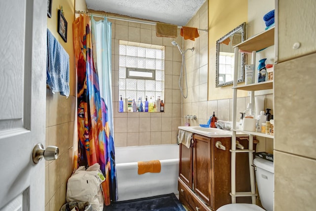 bathroom featuring tile walls, shower / bath combo with shower curtain, vanity, and a textured ceiling