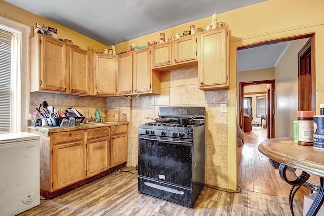 kitchen featuring light brown cabinetry, light countertops, light wood finished floors, backsplash, and black gas range