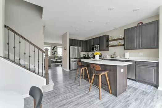 1672 Bentz Way, Batavia, IL 60510 - kitchen with appliances with stainless steel finishes, open shelves, light wood-style flooring, a breakfast bar, and light countertops