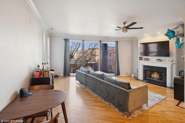 living area featuring a fireplace with flush hearth, crown molding, wood finished floors, and ceiling fan