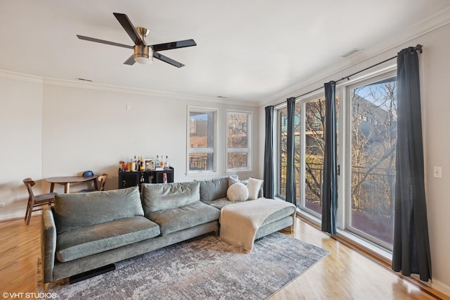 living room featuring baseboards, light wood-type flooring, crown molding, a ceiling fan, and visible vents