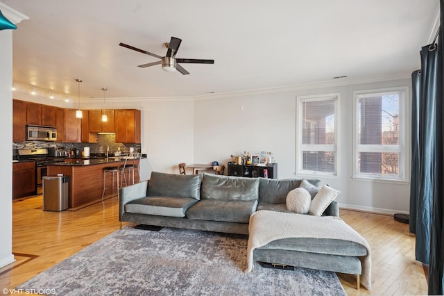 living area featuring ornamental molding, light wood-style flooring, a ceiling fan, and baseboards