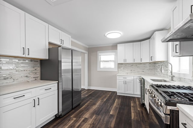 kitchen featuring light countertops, a sink, appliances with stainless steel finishes, dark wood-style floors, and wall chimney range hood