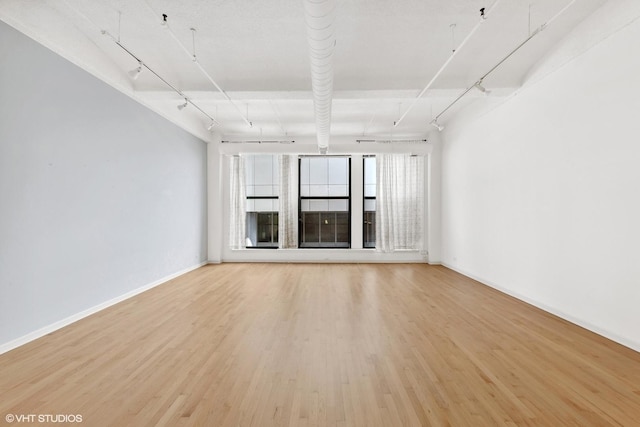 unfurnished living room with rail lighting, light wood finished floors, and baseboards