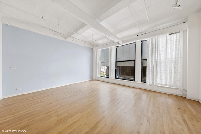 unfurnished room featuring track lighting, wood finished floors, and baseboards