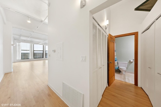hall featuring track lighting, light wood-style floors, baseboards, and visible vents
