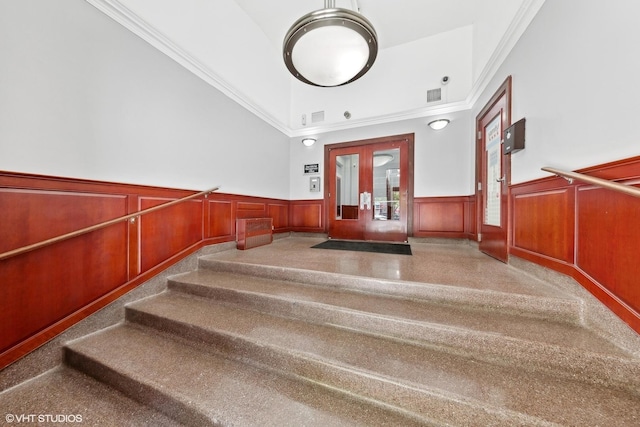stairs featuring crown molding, visible vents, and a wainscoted wall