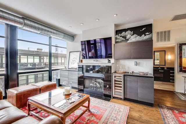 living area with visible vents, floor to ceiling windows, wood finished floors, and beverage cooler