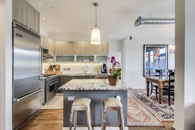 kitchen with modern cabinets, under cabinet range hood, a sink, high quality appliances, and a kitchen breakfast bar