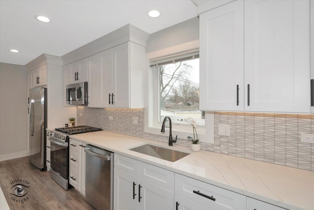 kitchen featuring stainless steel appliances, a sink, light stone counters, white cabinets, and wood finished floors