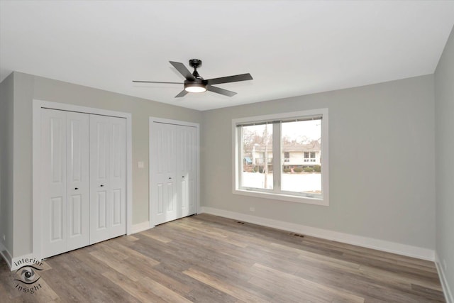 unfurnished bedroom featuring light wood-style flooring, baseboards, multiple closets, visible vents, and a ceiling fan