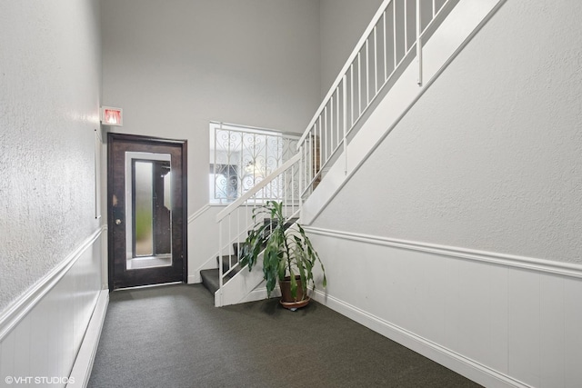 carpeted foyer with a textured wall, a towering ceiling, a wainscoted wall, and stairs