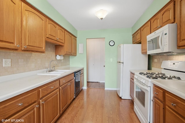 kitchen with a sink, light countertops, white appliances, brown cabinetry, and light wood-style flooring
