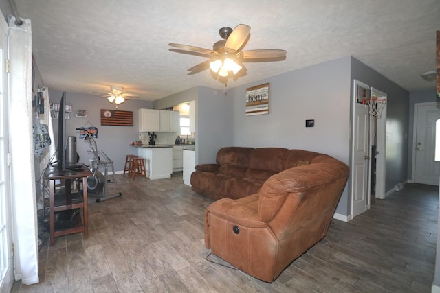 living room with ceiling fan, baseboards, light wood-style floors, and a textured ceiling
