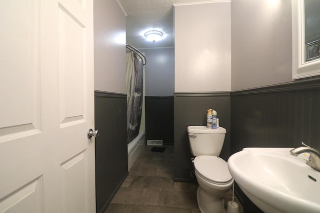 full bath featuring toilet, shower / bath combination with curtain, a sink, and wainscoting