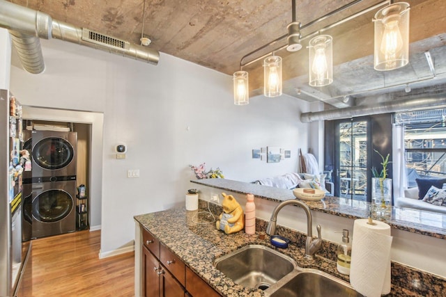 1070 W 15th St Unit 305, Chicago, IL 60608 - kitchen with stacked washer / drying machine, a sink, brown cabinetry, light wood-style floors, and dark stone countertops