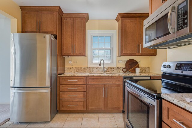 kitchen featuring brown cabinetry, stainless steel appliances, light stone countertops, and a sink