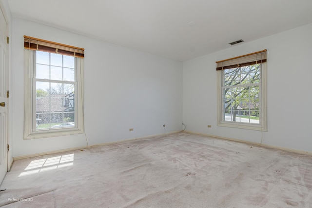 spare room with carpet flooring, visible vents, a wealth of natural light, and baseboards