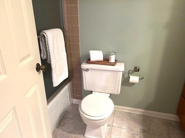 bathroom featuring baseboards, toilet, tile patterned flooring, and  shower combination