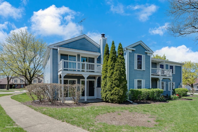 view of front of property featuring a chimney, a balcony, and a front lawn