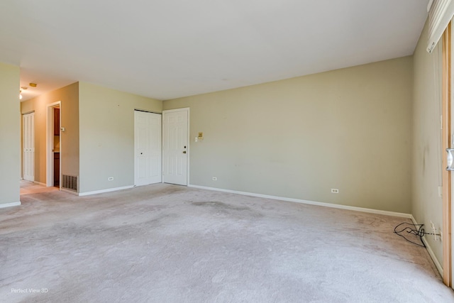 spare room featuring light colored carpet, visible vents, and baseboards