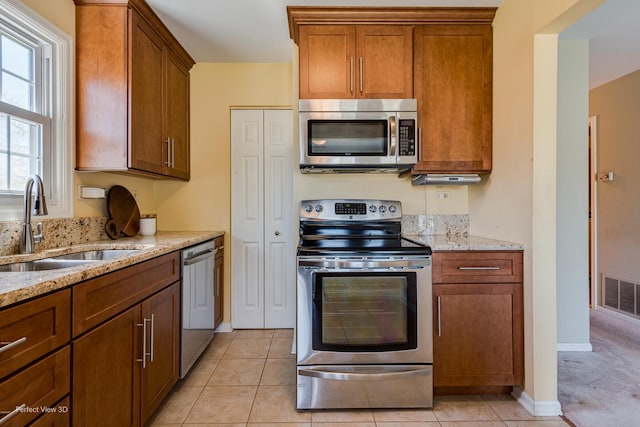 kitchen with brown cabinets, a sink, visible vents, stainless steel appliances, and light stone countertops