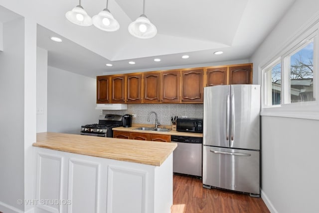 kitchen featuring light countertops, a peninsula, stainless steel appliances, tasteful backsplash, and a sink