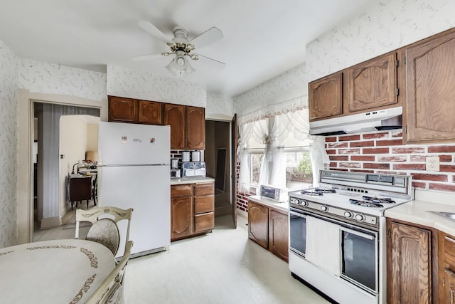 kitchen featuring light countertops, a ceiling fan, white appliances, under cabinet range hood, and wallpapered walls