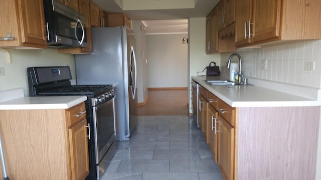 kitchen with tasteful backsplash, appliances with stainless steel finishes, light countertops, a sink, and brown cabinets