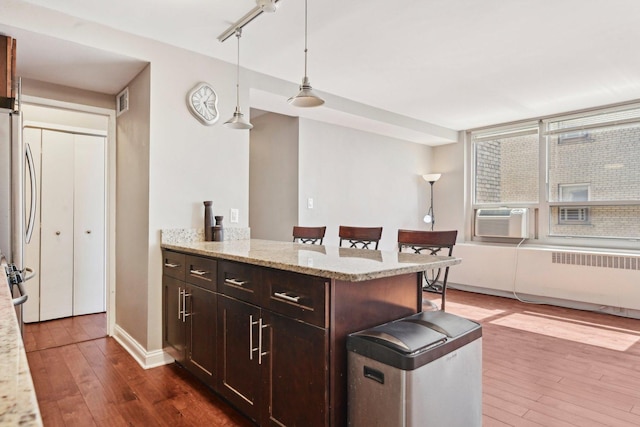kitchen with dark wood-style flooring, dark brown cabinets, pendant lighting, and radiator
