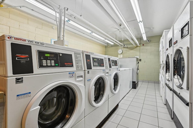 community laundry room featuring light tile patterned floors, washing machine and clothes dryer, and concrete block wall