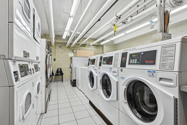 community laundry room featuring washing machine and dryer, stacked washer / drying machine, concrete block wall, and light tile patterned flooring