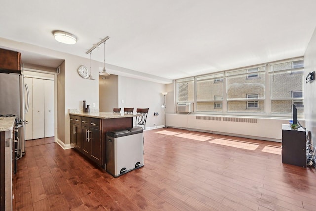 kitchen featuring dark brown cabinetry, light stone countertops, radiator, dark wood finished floors, and pendant lighting