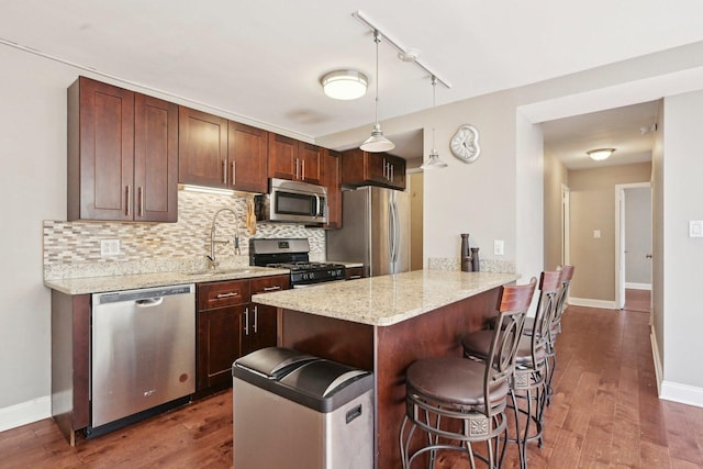 kitchen with tasteful backsplash, a breakfast bar, a peninsula, dark wood-type flooring, and stainless steel appliances