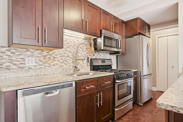 kitchen with backsplash, light stone countertops, dark wood-type flooring, appliances with stainless steel finishes, and a sink