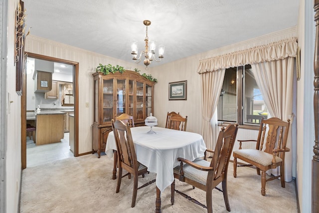 dining area featuring light colored carpet, a textured ceiling, a notable chandelier, and ornamental molding
