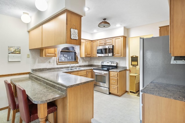 kitchen with a peninsula, dark countertops, stainless steel appliances, and a sink