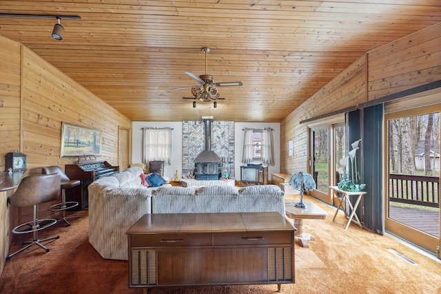 living room with wood ceiling, wood walls, carpet floors, and a wood stove