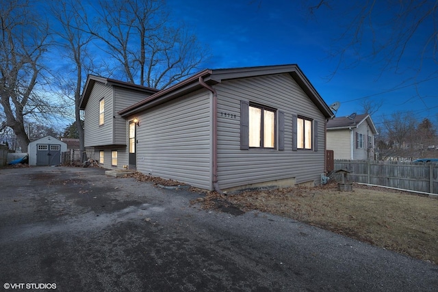 view of side of home with an outdoor structure, a shed, fence, and aphalt driveway