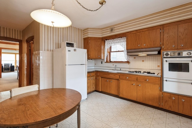 kitchen with light countertops, white appliances, wallpapered walls, under cabinet range hood, and a sink