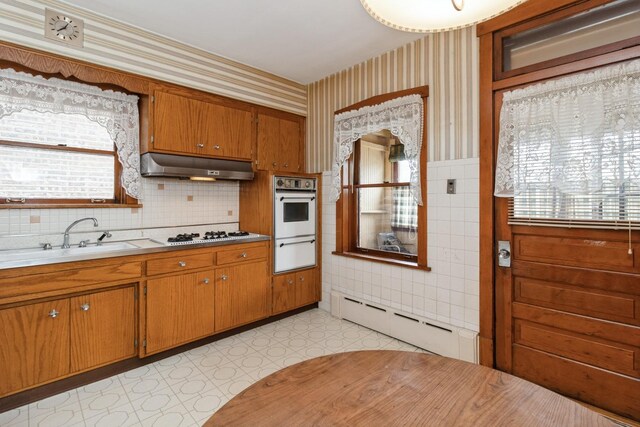 kitchen with white appliances, wallpapered walls, light floors, under cabinet range hood, and a sink