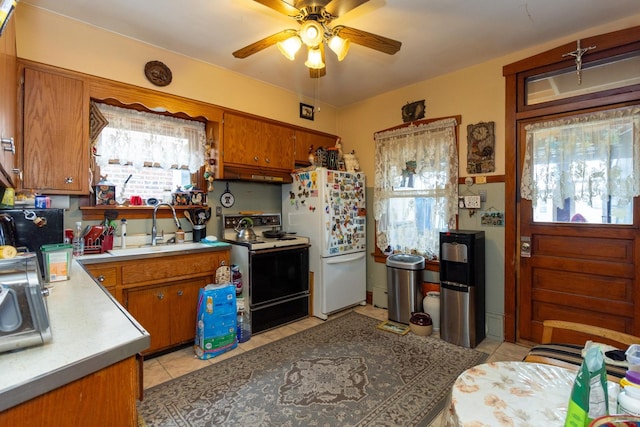 kitchen with freestanding refrigerator, a sink, brown cabinetry, and electric stove