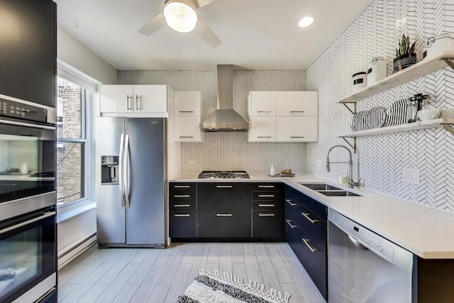 kitchen featuring stainless steel appliances, wall chimney exhaust hood, open shelves, a sink, and decorative backsplash