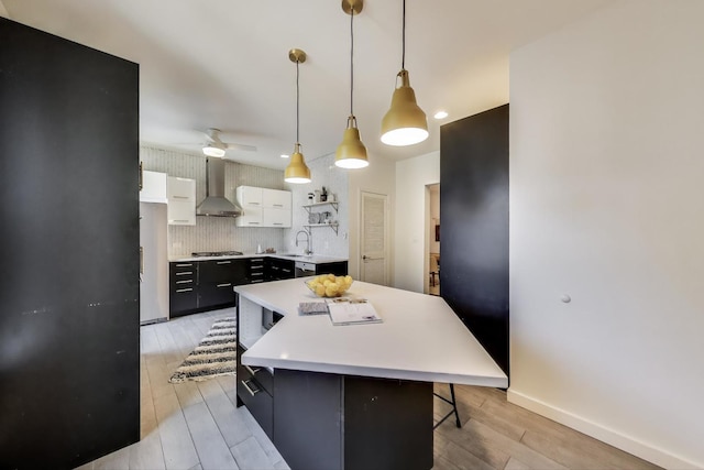 kitchen with wall chimney range hood, light countertops, gas stovetop, light wood-style flooring, and white cabinets