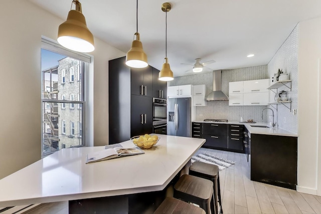 kitchen with wall chimney exhaust hood, appliances with stainless steel finishes, a sink, open shelves, and light countertops