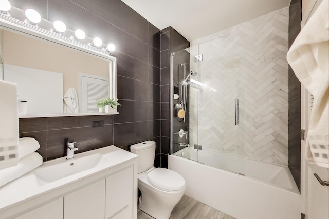 full bath featuring toilet, vanity, combined bath / shower with glass door, wood finished floors, and tile walls