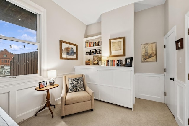 living area featuring light carpet, a wainscoted wall, built in features, and a decorative wall