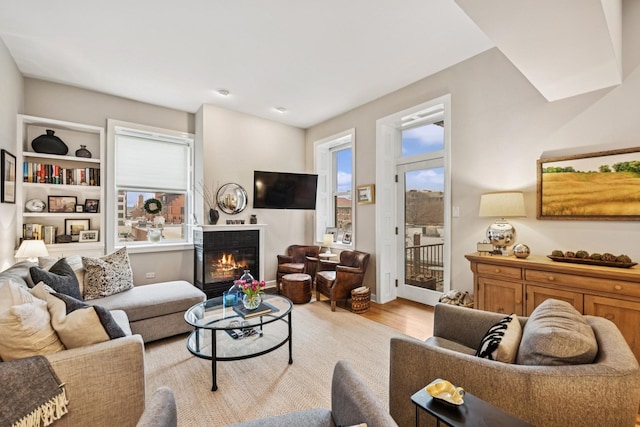 living room with light wood finished floors, plenty of natural light, and a glass covered fireplace